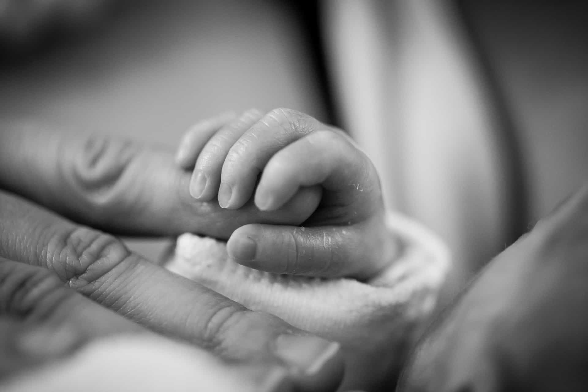 A mother holding a newborn baby's hand.