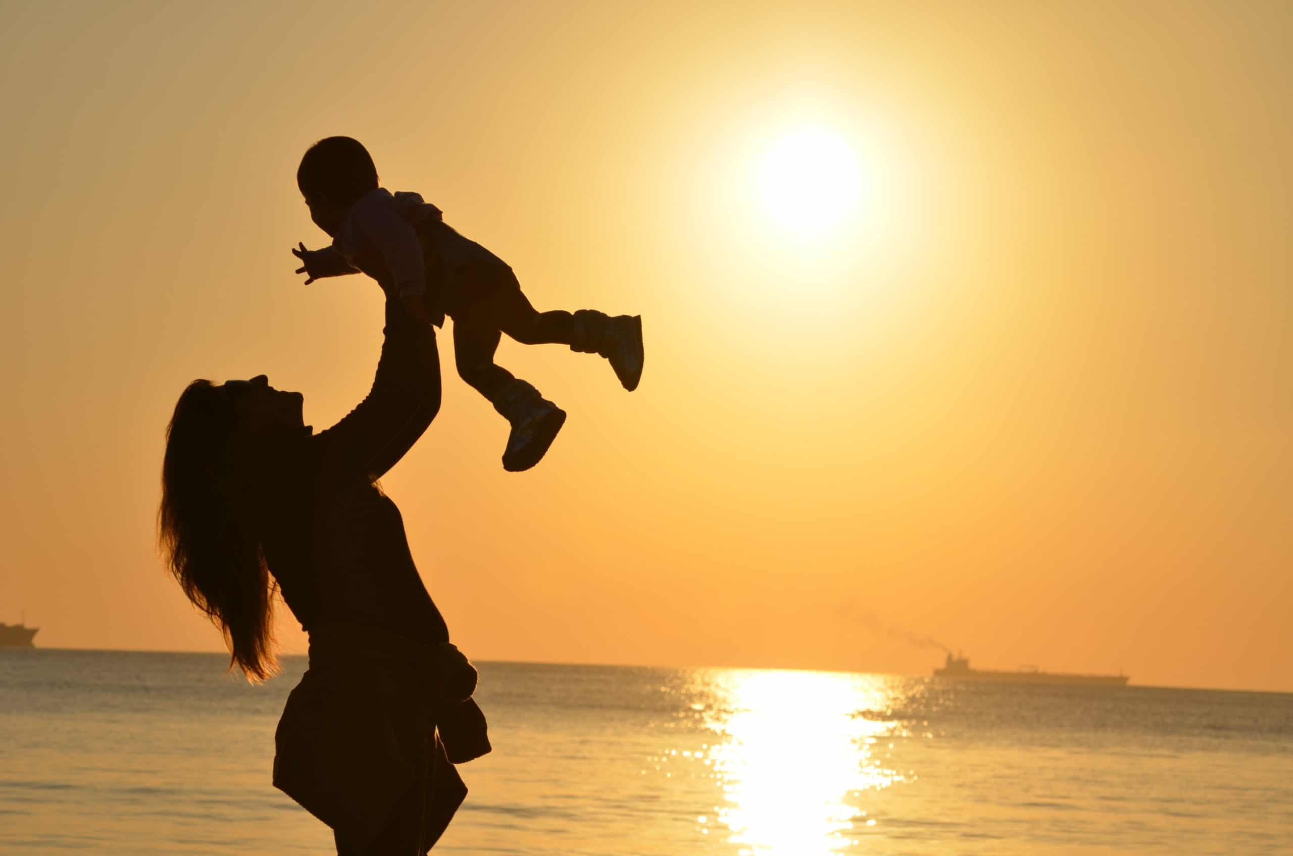 Mother holding her baby up in front of an ocean sunset