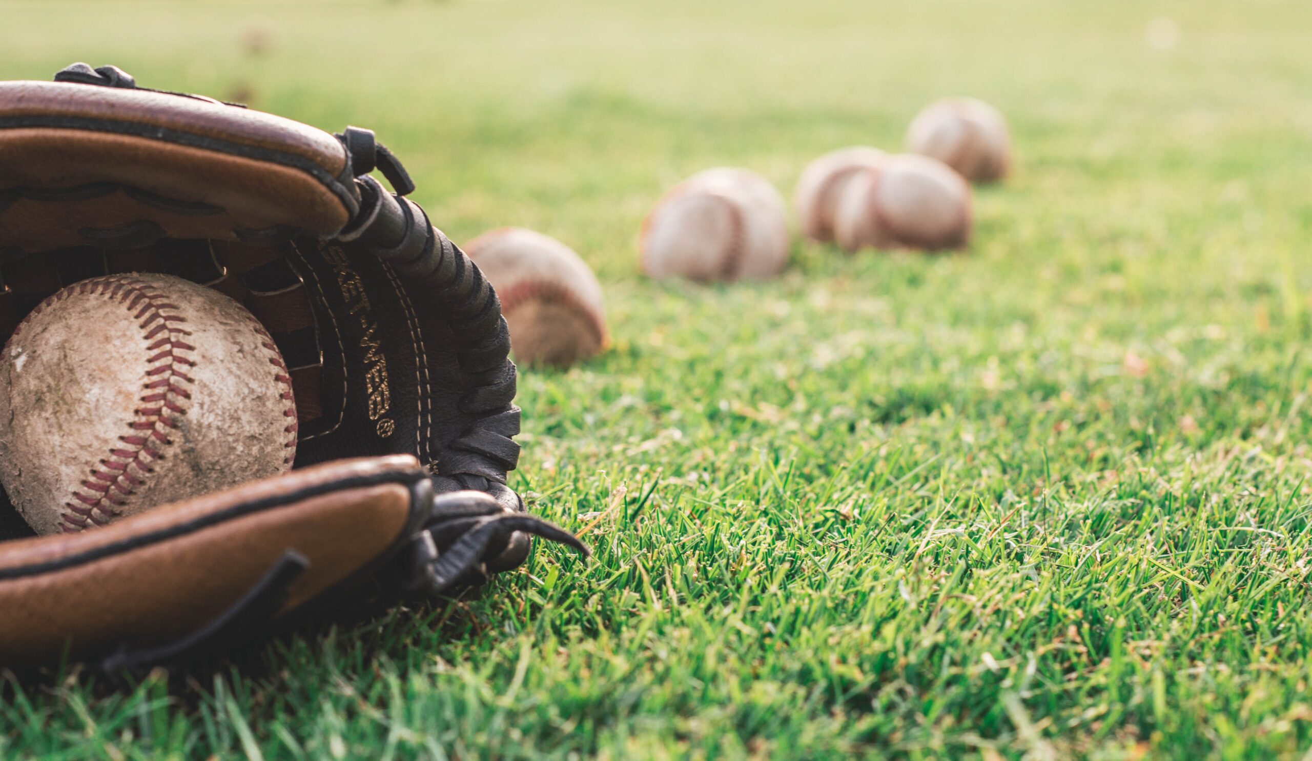 Baseballs and a glove laying on some grass