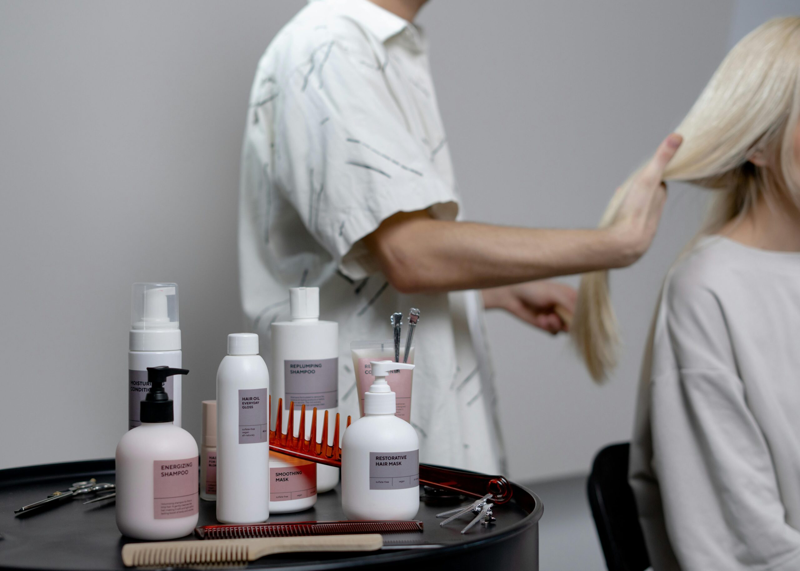 Man styling a woman's hair and a tray of hair products